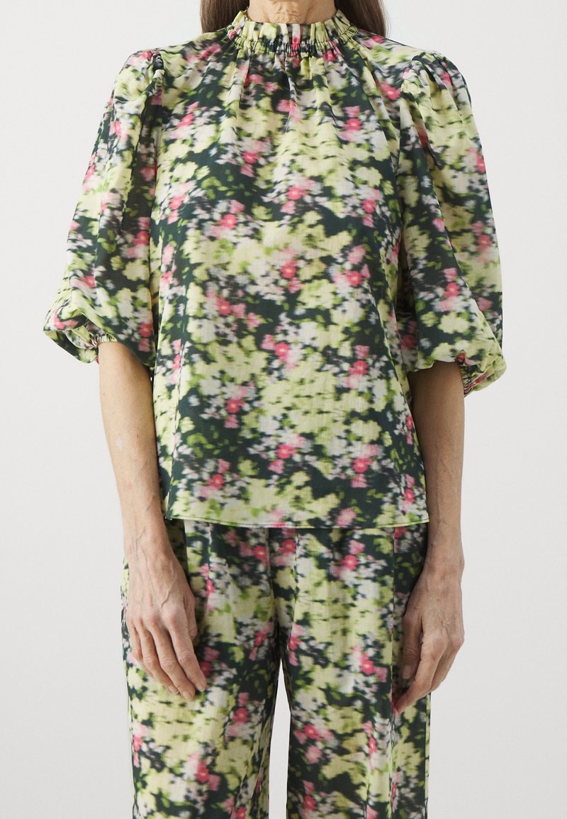 Femme portant un haut à motif floral avec des manches bouffantes et un pantalon assorti en vert, jaune, noir et rose.