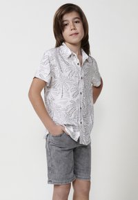 Balta trumpa rankovėmis marškiniai su pilkomis lapų raštais, derinami su pilkais džinsiniais šortais. Marškiniai turi apykaklę ir mygtukus.