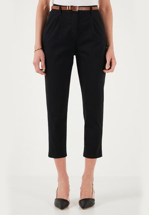 Zwarte high-waisted broek met een taps toelopende pijp, voorzien van voorplooien en een bruine riem. Gepaard met puntige zwarte hakken.