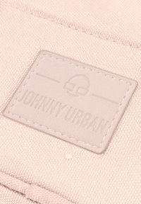 Světle růžová látka s texturovaným povrchem, která obsahuje vyšívanou koženou nášivku označenou "JOHNNY URBAN" s grafickým akcentem nad textem.