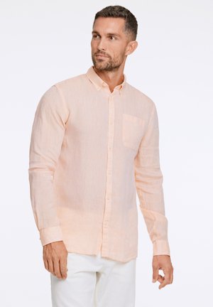 Camisa de botones de manga larga en color naranja claro, con tejido texturizado, que presenta un bolsillo en el pecho y un dobladillo ligeramente curvado. Combinada con pantalones blancos.