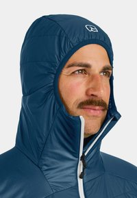 Marineblaue, isolierte Jacke mit hohem Kragen und Kapuze. Verfügt über einen Frontreißverschluss, gesteppten Textur und Logoakzent auf der Kapuze.
