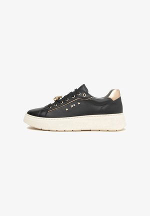 Zapatilla negra de cuero con suela gruesa blanca, acentos dorados en el talón, ojales, tachuelas decorativas y medallón en los cordones, detalle de logo lateral.