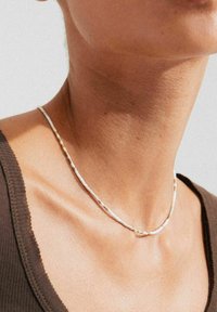 White bead necklace with gold accents, features a simple design, delicate shape, smooth texture, and evenly spaced metallic details.
