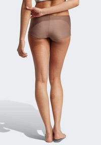 Hnědé boyshorts s hladkou texturou, středním pasem a jemným leskem. Holé nohy viditelné na neutrálním pozadí.