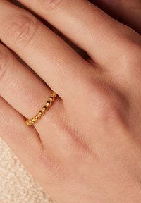 Gouden ring met kleine, gelijkmatig verdeelde bolvormige kralen. De band is glad en dun, gedragen op een lichte, gestructureerde hand.