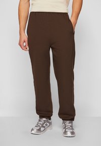 Pantaloni joggers din fleece maro, cu o talie elastică și buzunare laterale, având o croială relaxată și manșete ribbrate. Poartați cu pantofi sport argintii.