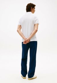 Hvid kortærmet polo t-shirt kombineret med mørkeblå bukser. Outfittet har en afslappet pasform, med let tekstur og kontrastdetaljer.