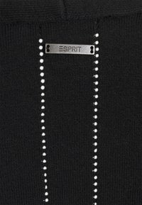 Czarna dzianina z pionowymi rzędami białych kropek. Metalowa zawieszka z logo "ESPRIT" przymocowana na górze, podkreślająca tożsamość marki.