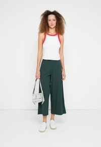 Débardeur blanc avec bretelles rouges, pantalon vert à jambes larges, baskets blanches et sac à main transparent. Design épuré avec un style décontracté contemporain.
