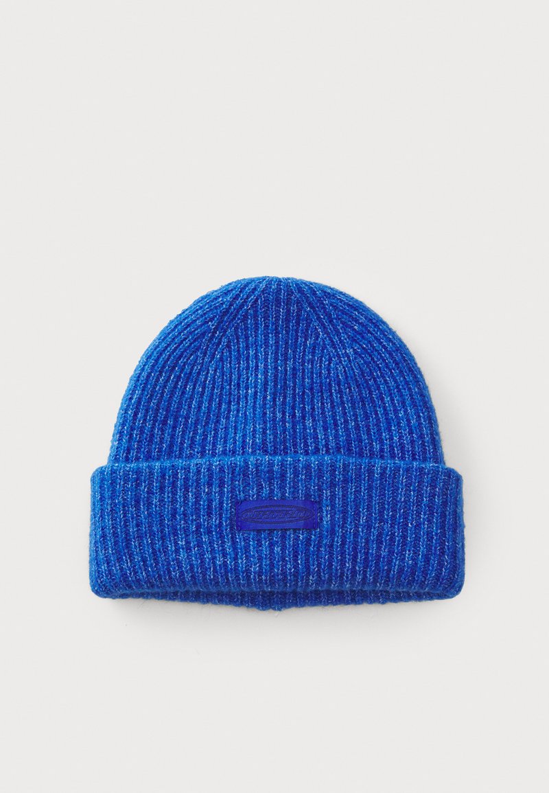 Cappello a cuffia blu a coste con orlo piegato e finitura testurizzata. Presenta una piccola etichetta logo viola sulla parte anteriore.