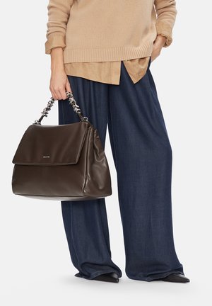 Osoba ubrana w beżowy sweter i granatowe szerokie spodnie, trzymająca dużą ciemnobrązową skórzaną torebkę z plecioną rączką.