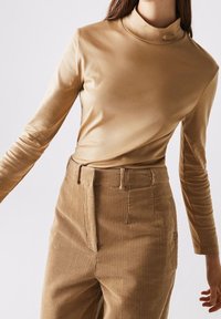 Long-sleeve, turtleneck top in light beige, made of smooth fabric; paired with corduroy pants featuring vertical stripes and a button detail.