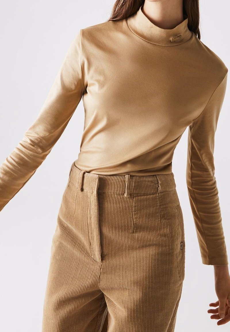 Long-sleeve, turtleneck top in light beige, made of smooth fabric; paired with corduroy pants featuring vertical stripes and a button detail.