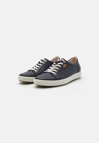 Navy blue sneakers with light grey soles, featuring round toes, white laces, a smooth texture, and a small tan logo detail on the side.