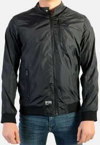 Sort bomberjakke lavet af let, skinnende materiale. Har lynlåslukning foran, to sidelommer og strikkede manchetter. Syning med label ved kanten.