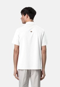 Camicia bianca a maniche corte con colletto, dotata di un piccolo accento della bandiera belga sul retro. Tessuto liscio e vestibilità rilassata.