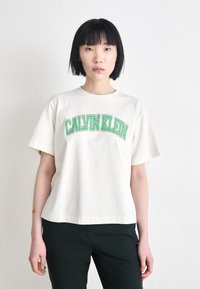 Hvid bomulds t-shirt med "CALVIN KLEIN" i grøn buet skrift, korte ærmer, en afslappet pasform og rund halsudskæring.