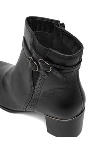 Črni gležnarji iz usnja z teksturirano površino, dvojnimi zaponkami in nizko blok peto; vključujejo stranski zadrgo in perforirane detajle.