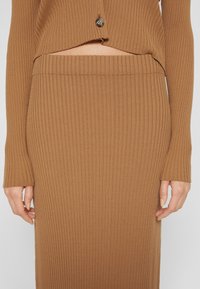 Femme portant une jupe en maille côtelée marron et un cardigan court assorti avec manches longues et fermeture à boutons.