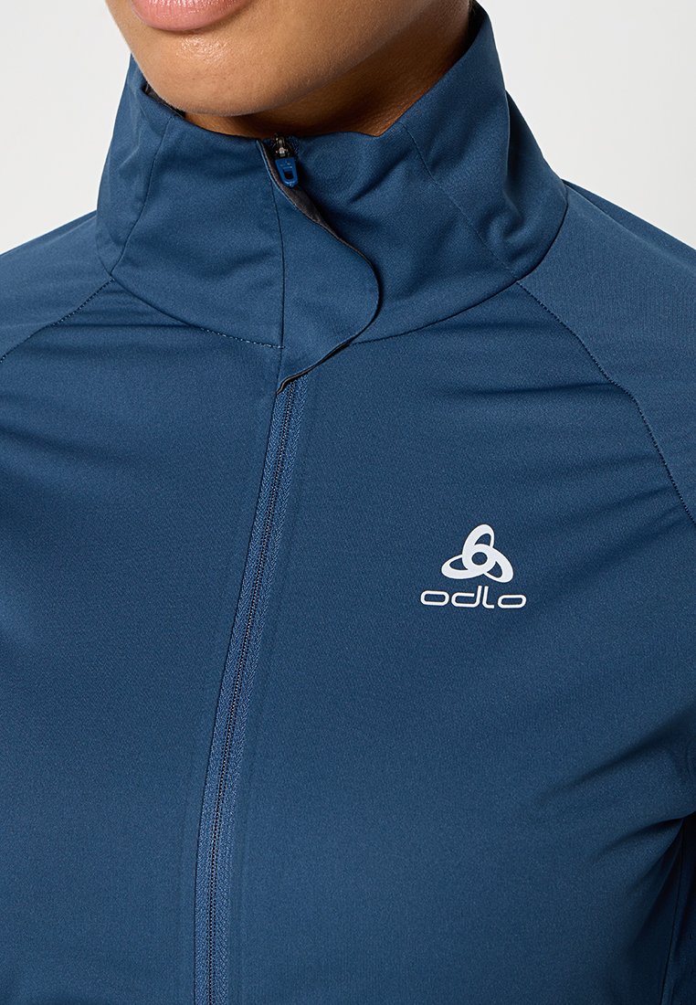 Marineblaue Performance-Jacke mit hohem Kragen, Viertelreißverschluss und weißen Logodetails. Hergestellt aus leichtem, dehnbarem Material für besten Tragekomfort.