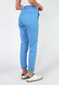 Lichtblauwe, slim-fit broek gemaakt van een soepele stof, met een opgerolde zoom en achterzak. Gecombineerd met wit-zwarte sneakers.