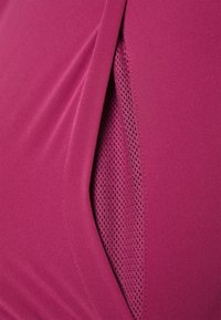 Gros plan d'un vêtement violet montrant une couche de tissu pliée et un panneau en mesh intérieur avec de petites perforations.