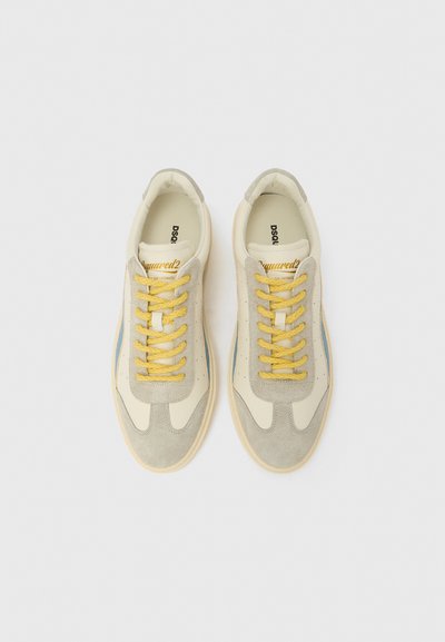 Tennised, mille ülaosaks on beež nahk, hallide seemisnahast detailidega, kollased paelad, sinised küljeribad ja tekstureeritud kummist tallad.