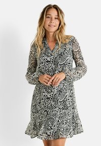 Vestido de manga larga en tejido translúcido con un patrón de paisley en blanco y negro, con escote en V y dobladillo con volantes, que ofrece una silueta fluida.
