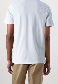 Helles blaues Rundhals-T-Shirt aus einem weichen Material, mit kurzen Ärmeln und geradem Saum, von hinten betrachtet. Taillierte Passform, minimalistisches Design.