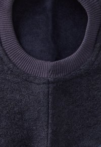 Granatowy sweter z okrągłym żebrowanym dekoltem. Teksturowany materiał o miękkim, puszystym wyglądzie i widocznych detalach szwów.