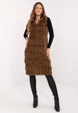 Braune Kunstfellweste mit Kapuze, mit einem strukturierten, vertikal gerippten Design, Reißverschluss vorne und wellenförmigem Saum. Getragen über schwarzen Leggings und Stiefeln.