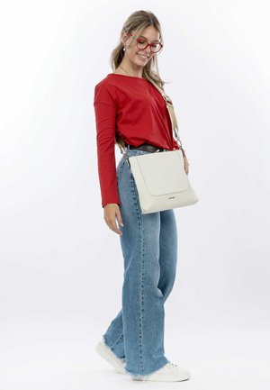 White leather shoulder bag with a smooth texture, featuring a flap closure and adjustable strap, paired with a red long-sleeve top and blue jeans.