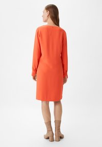 Helle orange Knielangkleid mit langen Ärmeln und geradem Schnitt; verfügt über einen dezenten Bootsausschnitt und elastische Bündchen.
