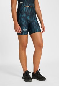 Höga midjade shorts med teal-färgat mönster och slät textur, med en logotyp på vänster ben. Matchas med svarta sportskor.