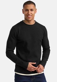 Camiseta negra de manga larga con cuello redondo y diseño ajustado de tejido acanalado, con un logo sutil en el pecho y un efecto de capas.