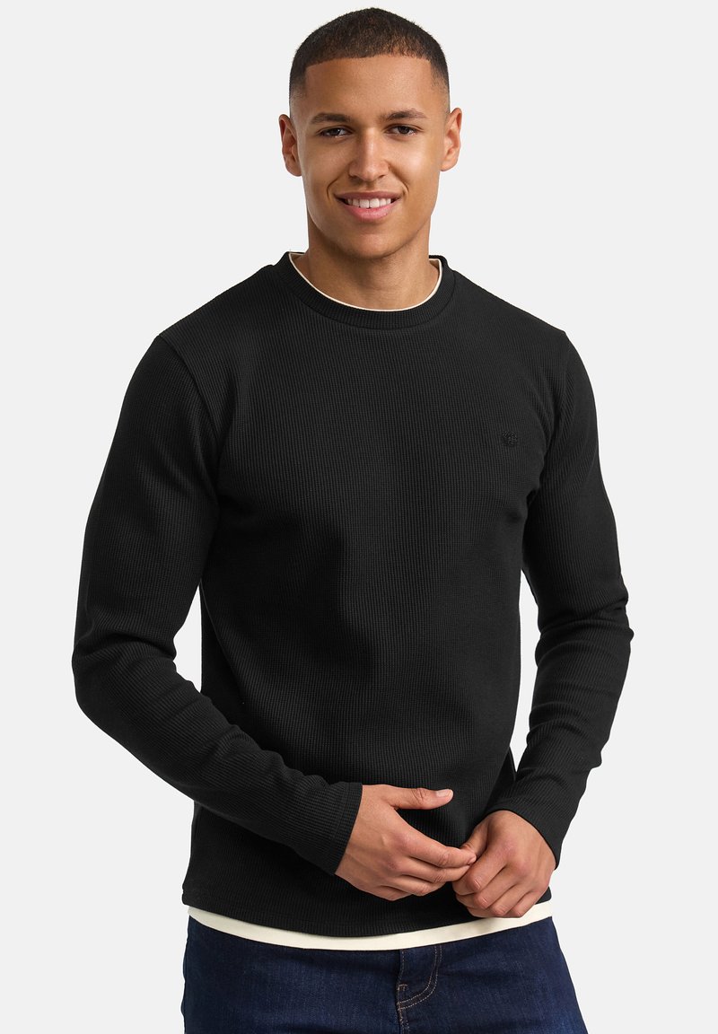 Camiseta negra de manga larga con cuello redondo y diseño ajustado de tejido acanalado, con un logo sutil en el pecho y un efecto de capas.