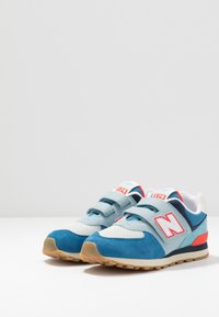 Baskets bleues et gris clair avec une empeigne en suede texturée, des accents rouges contrastants, des bandes Velcro et une semelle en caoutchouc.