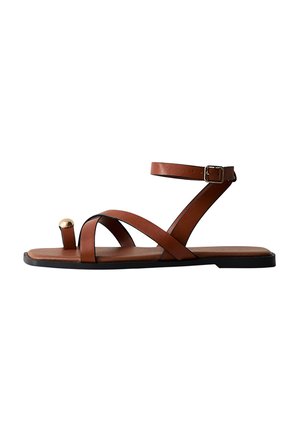 Bruine leren sandalen met een enkelriem, een gekruist bovenwerk, een platte zool en een gouden accent op de teenlus.