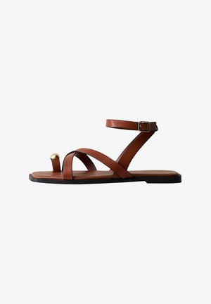 Sandale en cuir marron avec une lanière à la cheville, un dessus croisé, une semelle plate et un accent doré sur la boucle de l'orteil.