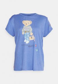 Modré tričko s krátkým rukávem se zvonkovým potiskem medvěda v mikině a džínech, s tištěným textem a malými barevnými akcenty.