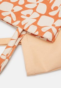 Gros plan de deux pochettes en tissu, une beige et une orange avec un motif floral abstrait blanc, montrant les bords cousus et des boucles en tissu.