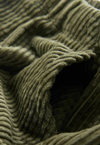Olivgrün gestreifter Stoff mit einer weichen, strukturierten Oberfläche, die prominent erhabene, wellenförmige Streifen aufweist.