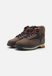 Scarponi da trekking marroni con tomaia in camoscio e tessuto, suola in gomma, sistema di allacciatura con accessori neri e colletto imbottito per il comfort.