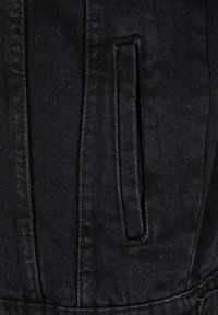 Közelkép fekete farmer anyagról, amely függőleges hasítékzsebbel és erősített varrással rendelkezik a széleken.