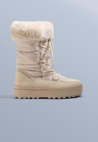 Beige winterlaars met bontvoering, gevoerde bovenkant, veterluiting, dikke zool en gestructureerde onderkant. Gladde materiaal met een strak design.