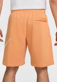 Pantalones cortos Nike naranja con una textura suave, cinturilla elástica, bolsillos laterales y un detalle del logo blanco en la pierna izquierda.