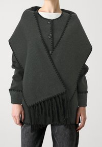 Poncho grigio scuro con orlo frangiato, chiusura a bottone e bordo a zigzag. Realizzato in morbido tessuto testurizzato con una vestibilità rilassata.