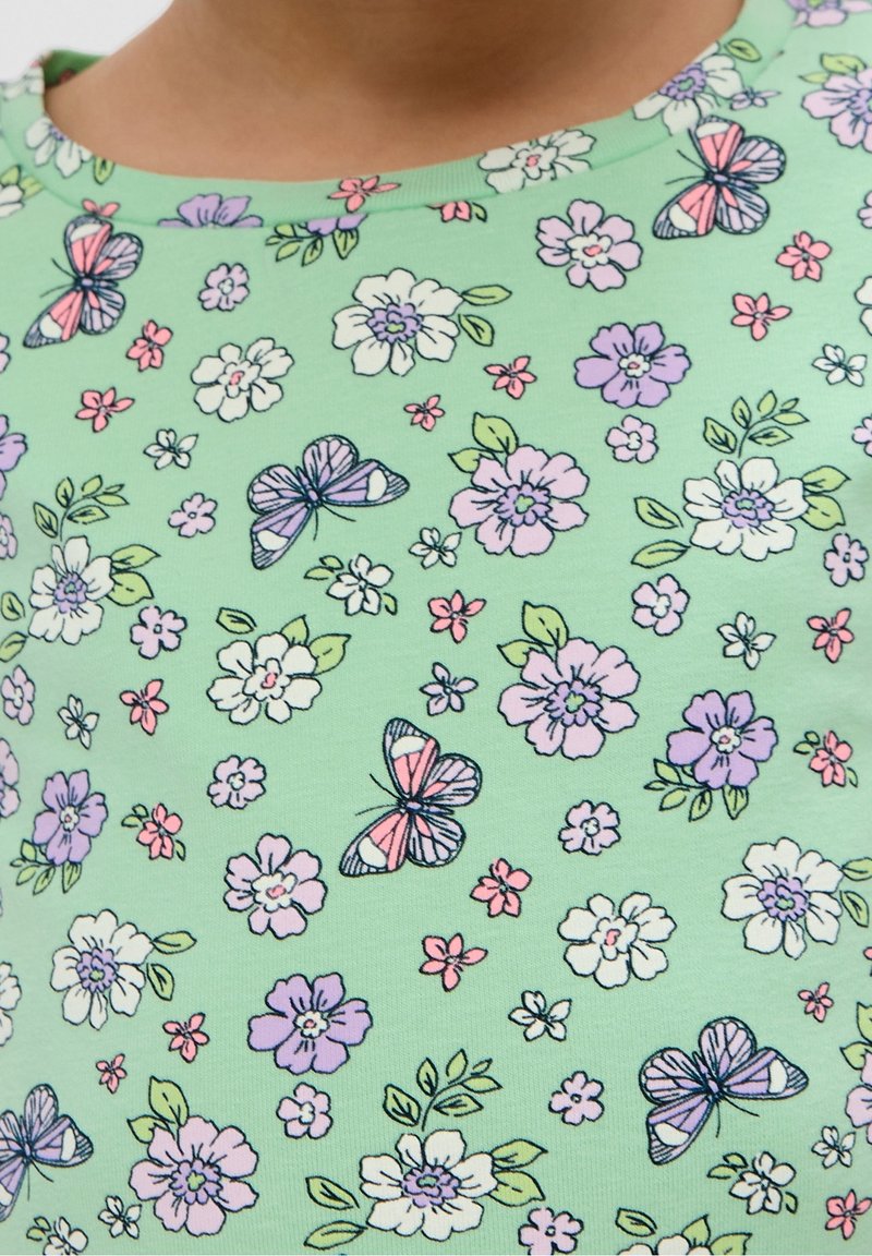Chemise verte pour enfant avec des fleurs roses, violettes et blanches ainsi que des papillons imprimés en motif dispersé.