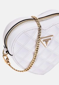 Hvid hjerteformet håndtaske lavet af glat syntetisk materiale. Den har et quiltet mønster, guld kædestrop og fremtrædende logodetalje.